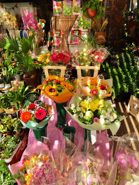 A display of fresh floral bouquets arranged on dark green pedestal stands and beige baskets in a flower shop. The bouquets feature bright, colorful flowers such as yellow sunflowers, pink gerbera dais